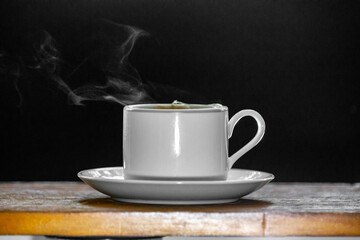 Minimalist cup of tea coming out of smoke on wooden surface and dark background.