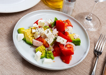 Diet salad consisting of pieces of tomato, avocado, cut onion and cheese dished up in a plate