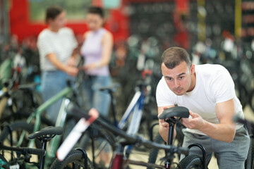 Interested avid cyclist choosing new bike for cycling trips in busy store, carefully picking...