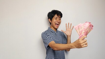 Young Asian man is happy to pose holding money and showing the 5 finger say hi pose