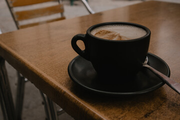 A black coffee cup, mug stands on an old wooden table. Aromatic tasty cappuccino or cocoa in a cafe. Aromatic and hot morning beverage in cafeteria.