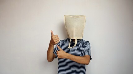 young Asian man wearing a shopping bag on his head with an okay hand gesture