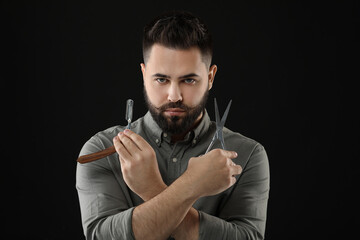 Handsome young man with mustache holding blade and scissors on black background