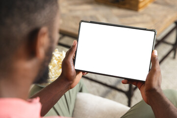 African American man holding a tablet with a blank screen at home with copy space