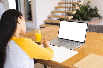A biracial young woman wearing yellow top, working on a laptop at home, copy space - Powered by Adobe