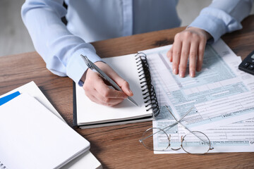 Payroll. Woman taking notes in notebook while working with tax return forms at wooden table, closeup