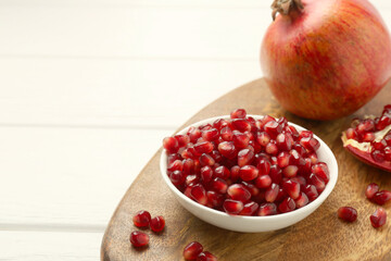 Ripe juicy pomegranate grains on white wooden table. Space for text