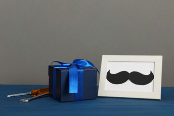 Happy Father's Day. Gift box, tools and frame with mustache on blue wooden table