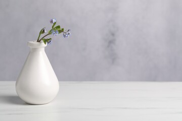 Beautiful forget-me-not flowers in vase on white marble table. Space for text