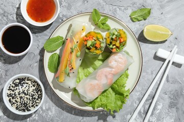 Tasty spring rolls served on grey textured table, flat lay