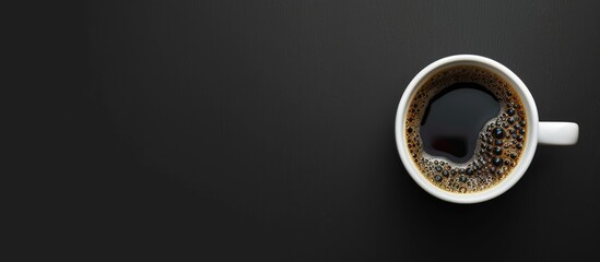 A white glass contains black coffee, set against a black backdrop, captured from above with space...