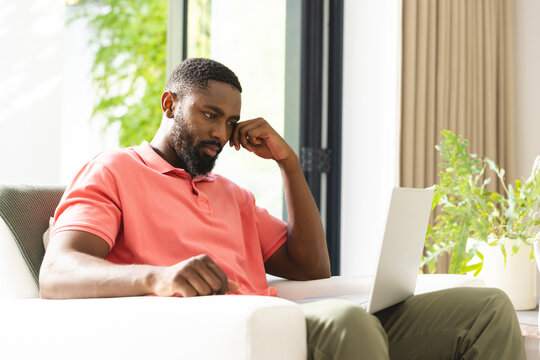 At home, African American man in pink shirt and green pants examining laptop screen