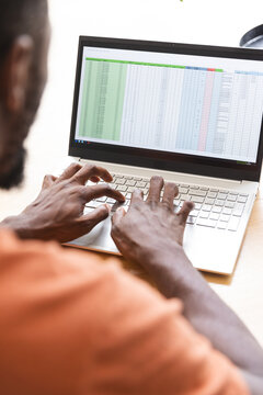 At home, African American male homeowner typing on laptop, viewing a spreadsheet