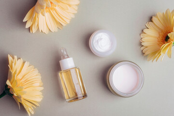 Cosmetic serum bottle, cream jars and yellow gerbera flowers on grey background. Top view, flat lay