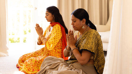 Indian mother and teenage daughter, sitting cross-legged at home, praying together