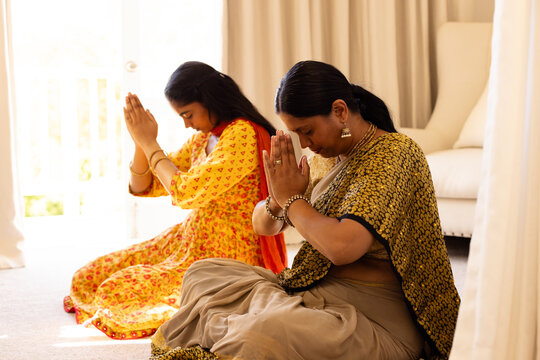 Indian mother and teenage daughter, wearing traditional clothes, praying together at home