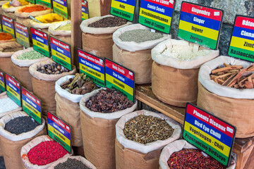 A colorful display of spices and herbs, including cumin, coriander, and ginger. The spices are...