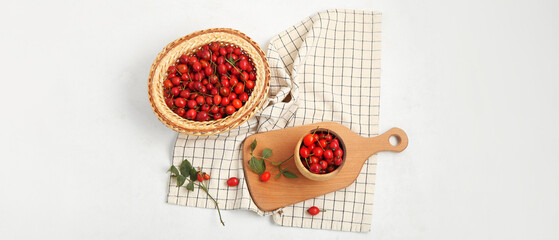 Bowl and wicker basket with fresh rose hip berries on white background