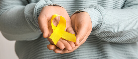 Woman holding golden ribbon on white background, closeup. Childhood cancer awareness concept