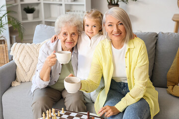 Little girl with her grandmother and great-grandma drinking tea at home