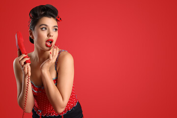 Shocked young pin-up woman with phone receiver on red background