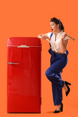 Shocked young pin-up worker with wrenches and retro fridge on orange background