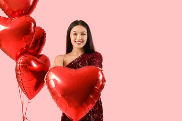 Young Asian woman with heart-shaped air balloons on pink background. Valentine's day celebration