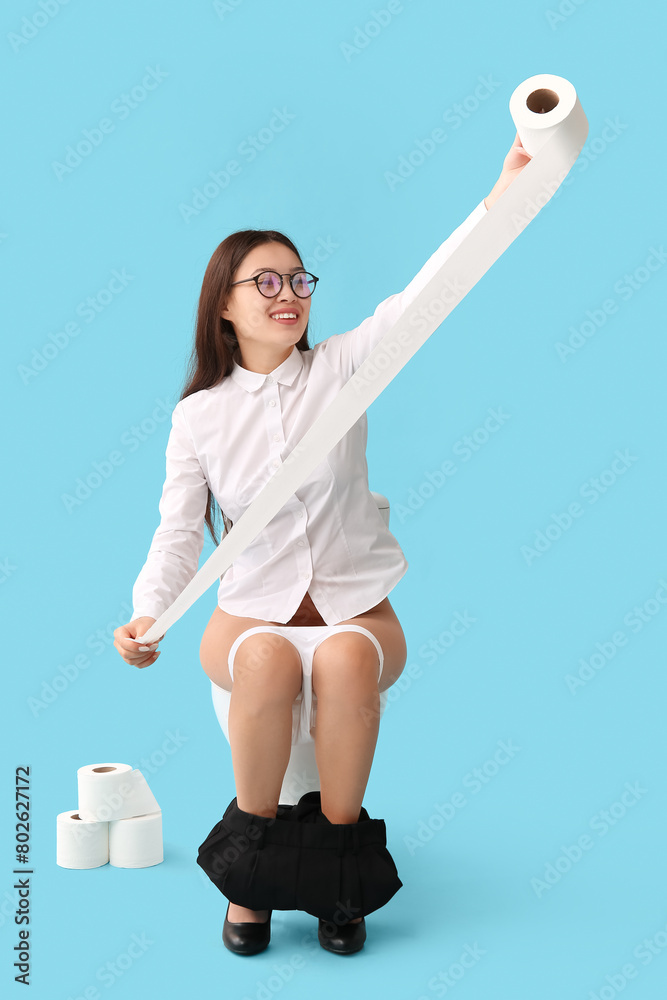 Poster Young Asian businesswoman with paper roll sitting on toilet bowl against blue background