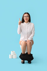 Young Asian businesswoman on toilet bowl pointing at something against blue background