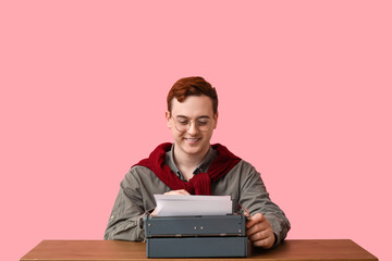 Young man with vintage typewriter at table on pink background