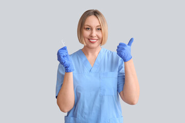 Female dentist with dental floss pick showing thumb-up on grey background