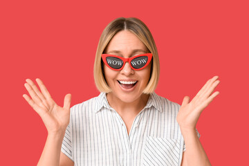 Surprised adult woman in eyeglasses with words WOW on red background