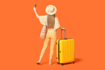 Young woman with suitcase, raising up her hand with passport on orange background. Travel concept. Back view