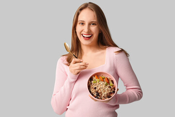 Happy young woman with bowl of healthy oatmeal on grey background