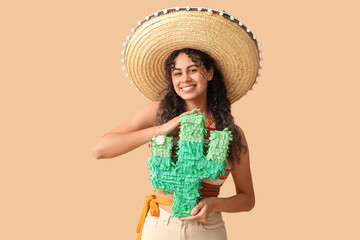 Beautiful young African-American woman in sombrero hat with pinata in shape of cactus on brown background