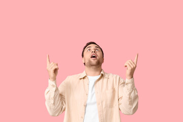 Young shocked man pointing at something on pink background