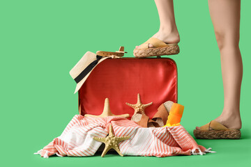 Legs of beautiful young woman near opened suitcase on green background