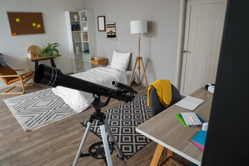 Interior of student's bedroom with table and telescope