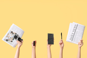 Female hands with newspapers, photo camera, notebook and pen on yellow background
