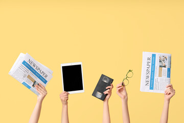 Female hands with newspapers, tablet computer, video cassette and eyeglasses on yellow background