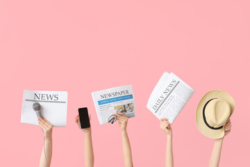 Female hands with newspapers, hat, microphone and mobile phone on pink background