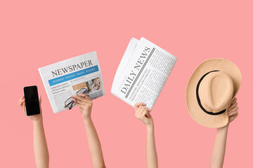 Female hands with newspapers, hat and mobile phone on pink background