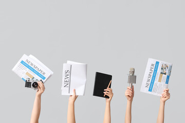 Female hands with newspapers, notebook, microphone and photo camera on grey background