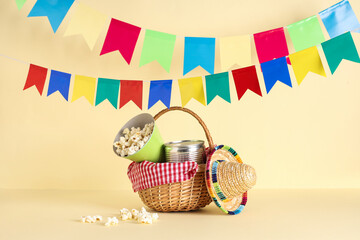 Wicker basket with popcorn, canned corn, mini sombrero and flags for Festa Junina celebration on...
