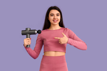 Sporty young woman pointing at percussive massager on lilac background