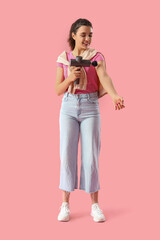 Young woman massaging her arm with percussive massager on pink background