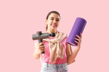 Young woman with percussive massager and foam roller on pink background