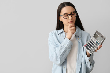 Thoughtful young woman with calculator on grey background