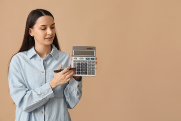 Beautiful young woman with calculator and pen on brown background