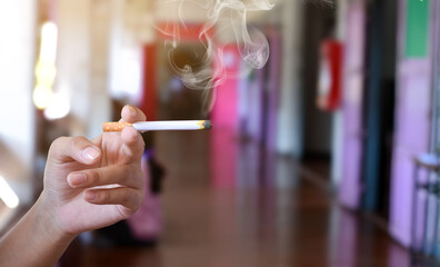 Hand holding lighted cigarette with smoking in front hallway of secondary school, concept for smoking problems in educational area.